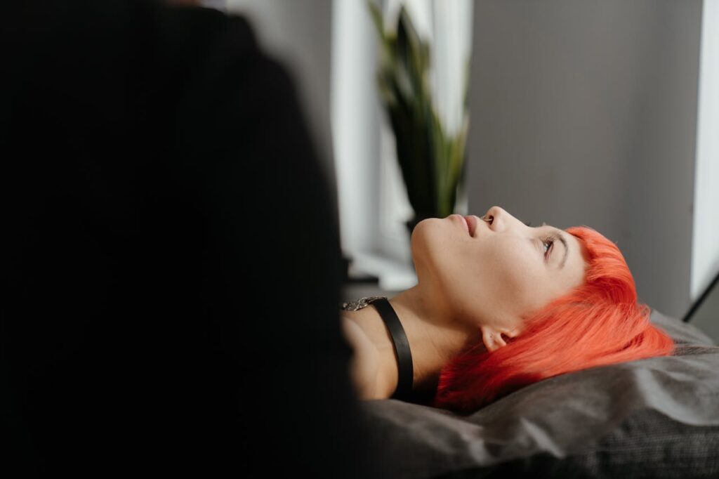 pexels-photo-4123820 Side profile of a young woman with vibrant red hair lying down in a tattoo studio.
